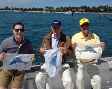 Three men holding the Blue Marlin flag on deck