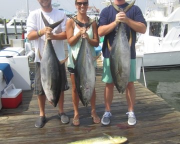 Three people holding three tuna on deck